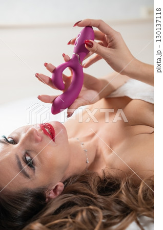 Caucasian woman in Santa Claus costume on bed holding curved sex toy.  130137118