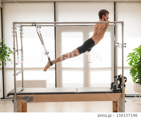 A man performs aerial exercises on a reformer machine. 130137146