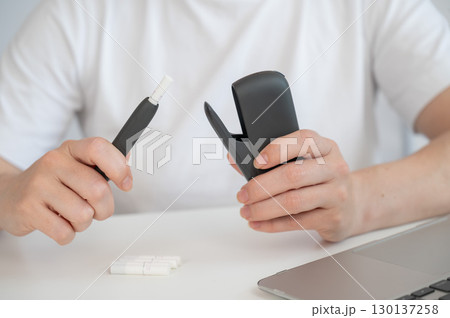 A woman takes a tobacco heating system out of a charger. Electronic cigarette. A woman takes a tobacco heating system out of a charger. Electronic cigarette. 130137258