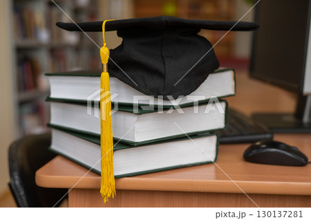 Graduation cap on a stack of books in the library. Graduation cap on a stack of books in the library. 130137281