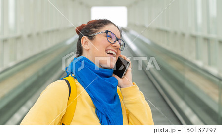 Happy woman stands on a travelator and talks on a cell phone 130137297