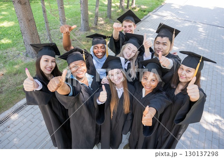 Students of different nationalities in graduation gowns give thumbs up.  130137298