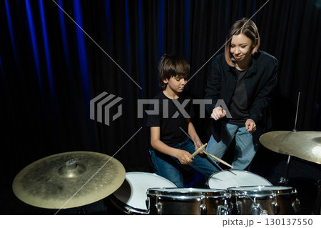 Young caucasian woman teaches a boy to play the drums in the studio on a black background. Music school student Young caucasian woman teaches a boy to play the drums in the studio on a black background. Music school student 130137550