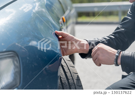 Caucasian man examines and tries to fix a deformation on the body of his car.  130137622