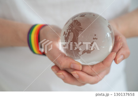 Woman wearing rainbow flag bracelet holding glass globe.  130137658