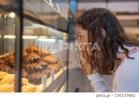 Caucasian woman looks greedily at baked goods in a bakery.  130137662