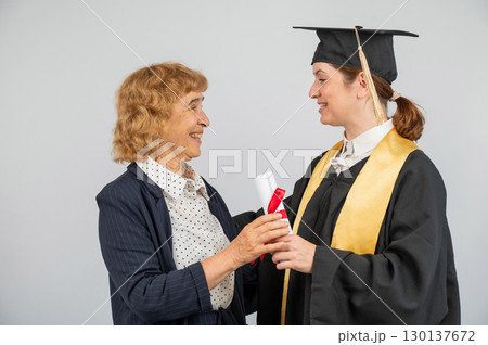 Portrait of Caucasian woman in graduation gown with her mother.  130137672