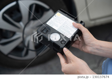 Woman holding a car tire pump. Woman holding a car tire pump. 130137674