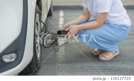 A woman pumps up a tire on a car.  130137729