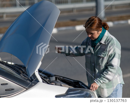 Caucasian female driver checking oil level in car engine.  130137763