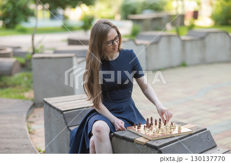 Caucasian woman playing chess outdoors. 130137770