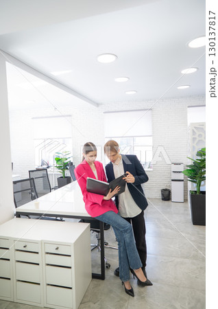 Colleagues look at a folder with documents and discuss work issues. Colleagues look at a folder with documents and discuss work issues. 130137817