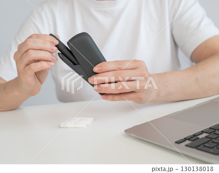 A woman takes a tobacco heating system out of a charger. Electronic cigarette. 130138018