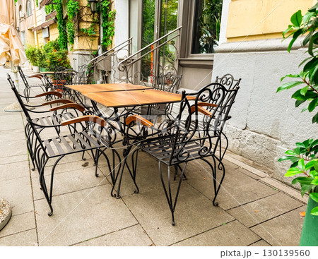 Outdoor cafe terrace with wooden tables and decorative metal chairs near old building. Restaurant, hospitality, lifestyle, urban culture and street dining. Outdoor cafe terrace with wooden tables and decorative metal chairs near old building. Restaurant, hospitality, lifestyle, urban culture and street dining. 130139560