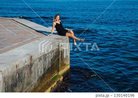 Blonde in a black dress walking on the beach by the sea Blonde in a black dress walking on the beach by the sea 130140196