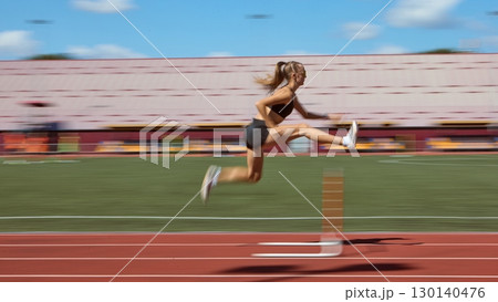 Dynamic blurred shot of female hurdler mid-air during race on stadium track 130140476
