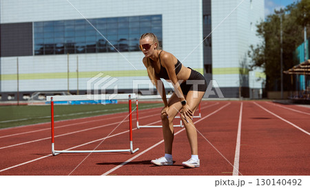 Female hurdler bending with exhaustion after intensive training on track 130140492