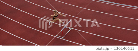 Female athlete hurdling viewed from above on red track. Banner 130140513