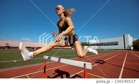 Young female athlete hurdling with speed and focus on outdoor track 130140517