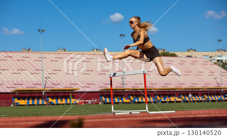 Strong woman athlete in flight above hurdle during stadium race 130140520