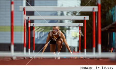 Female hurdler in starting position focused on race 130140535