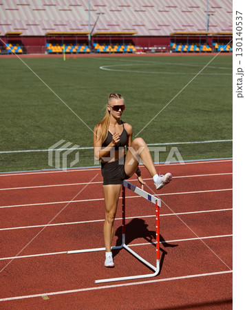 Female hurdler stretching leg on hurdle during training 130140537