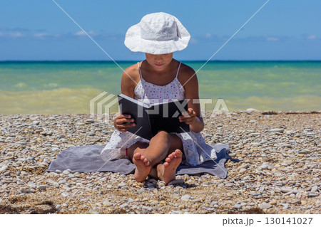 Child reading book on pebble beach Child reading book on pebble beach 130141027