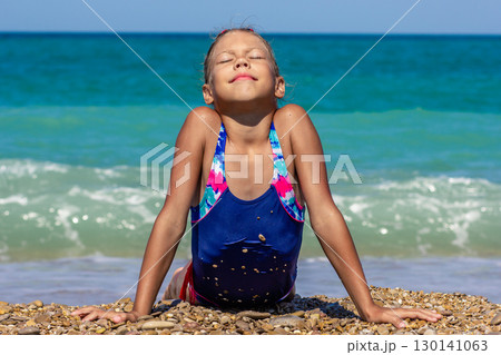 Girl lying on the beach, stretching toward the sun with closed eyes, enjoying the sunshine 130141063
