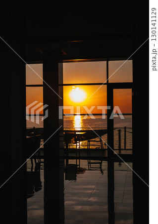 A beautiful sunset over the ocean, viewed from inside a building through the panoramic window. The setting sun casts a golden glow over the sea, seen through a window from inside the restaurant resort 130141129