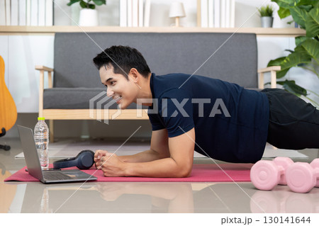 Home Workout. Young man smiling while doing plank exercise with laptop. Home Workout. Young man smiling while doing plank exercise with laptop. 130141644