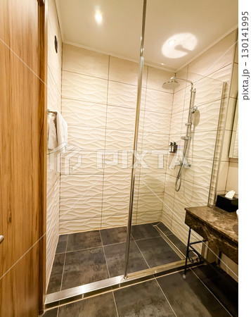 Walk-in shower with modern design and tiled walls. Cleanliness, hygiene, and comfort in hotel accommodation. 130141995