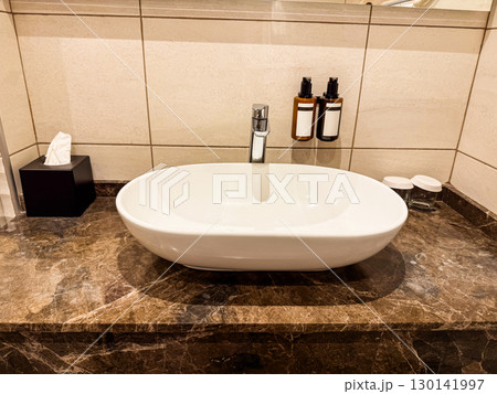Close-up of bathroom sink with marble countertop. Cleanliness, hygiene, and modern hospitality in travel accommodation. 130141997