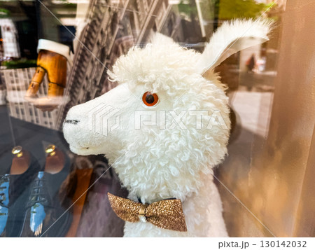 White plush toy llama with curly fur and golden bowtie in shop window display. Cute accessory, children toy, lifestyle, commercial retail and decorative product. 130142032