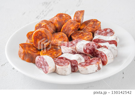 Assorted Spanish Chorizo and Fuet Sausage Slices on Minimal White Background Assorted Spanish Chorizo and Fuet Sausage Slices on Minimal White Background 130142542