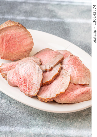 Perfectly sliced roast beef medium rare with seared crust on white plate 130142574