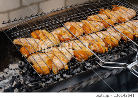 Delicious chicken frying on barbecue grill grate outdoor. Seasoning falling on fresh grilled chicken wings. Summer party food ideas. BBQ Juicy roasting chicken grill legs Delicious chicken frying on barbecue grill grate outdoor. Seasoning falling on fresh grilled chicken wings. Summer party food ideas. BBQ Juicy roasting chicken grill legs 130142641