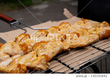 Delicious chicken frying on barbecue grill grate outdoor. Seasoning falling on fresh grilled chicken wings. Summer party food ideas. BBQ Juicy roasting chicken grill legs Delicious chicken frying on barbecue grill grate outdoor. Seasoning falling on fresh grilled chicken wings. Summer party food ideas. BBQ Juicy roasting chicken grill legs 130142642