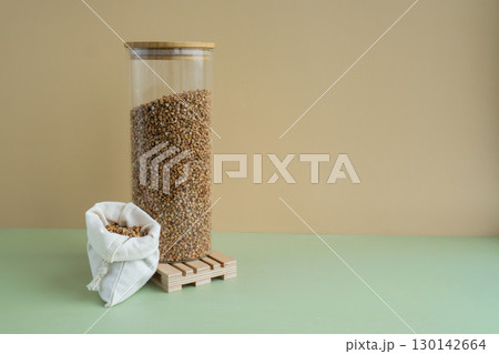 Refillable glass jar with raw buckwheat porridge and cotton bag. Copy space Refill product format eco-friendly living. Filling reusable container Whole spelt grain species. High protein fiber-rich 130142664