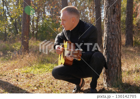 Portrait of smiling caucasian artist plays wooden acoustic guitar in autumnal park. Young songwriter plays string musical instrument hobby outside in nature fall time. Audio music healing 130142705