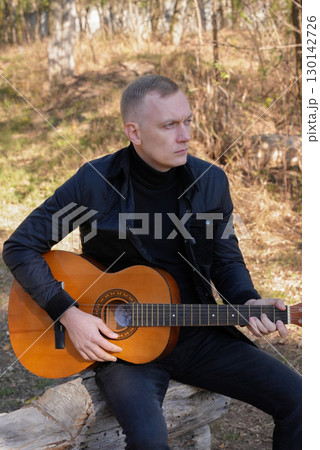 Blonde man playing string guitar outdoors in autumn forest. Concept of sound therapy, mental health and wellness rituals. Calmness tranquility audio-sensory practices. Aura farming energy 130142726