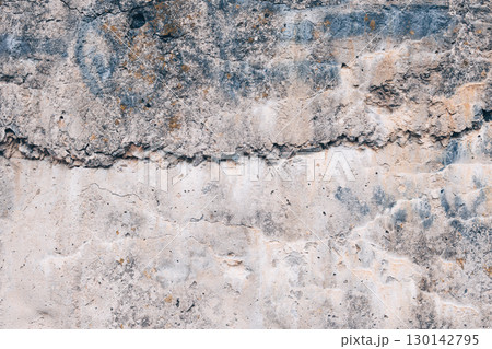 A fragment of the rough texture of an old concrete surface with cracks, stains and layers of weathered material. Gray-beige shade, pronounced relief and wear. Texture of a concrete wall. A fragment of the rough texture of an old concrete surface with cracks, stains and layers of weathered material. Gray-beige shade, pronounced relief and wear. Texture of a concrete wall. 130142795