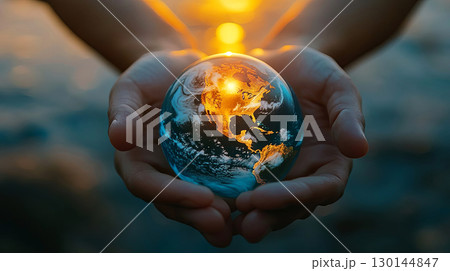 Hands gently cradling a glowing globe, symbolizing environmental awareness and global unity, with a warm sunset illuminating the scene, reflecting hope and connection to the Earth 130144847