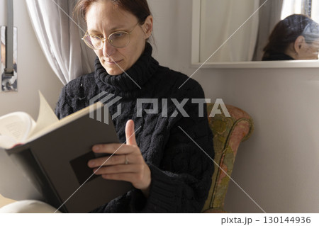 Woman reading a book while sitting on an armchair at home Woman reading a book while sitting on an armchair at home 130144936