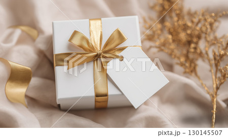 Christmas and New Year mockup of white gift box with blank tag on festive background and copy space, gold color tone. 130145507