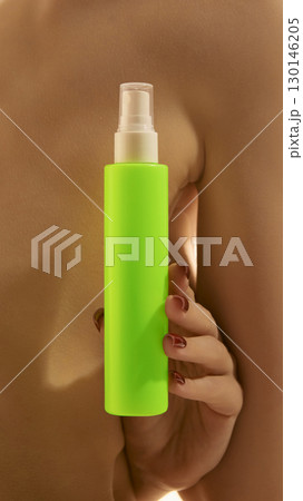 Bright neon green spray bottle held by female hand near body 130146205