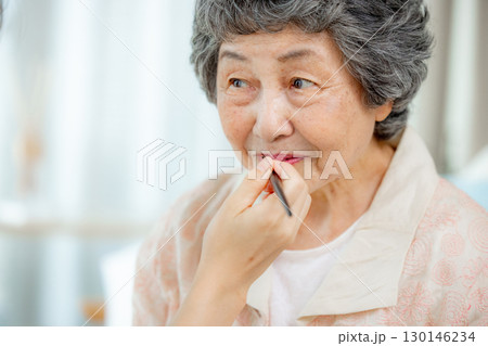 リビングで口紅を塗ってもらうシニア女性 130146234