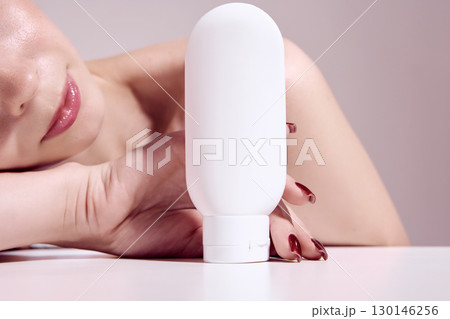 Woman with glossy lips holding white cosmetic bottle in hand for skincare and beauty branding Woman with glossy lips holding white cosmetic bottle in hand for skincare and beauty branding 130146256