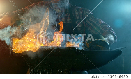 The blacksmith manually forging the molten metal on the anvil in smithy with spark fireworks 130146480