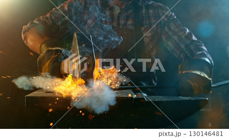 The blacksmith manually forging the molten metal on the anvil in smithy with spark fireworks 130146481