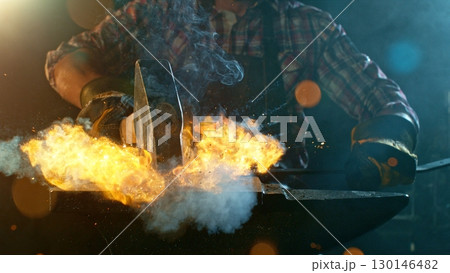 The blacksmith manually forging the molten metal on the anvil in smithy with spark fireworks 130146482